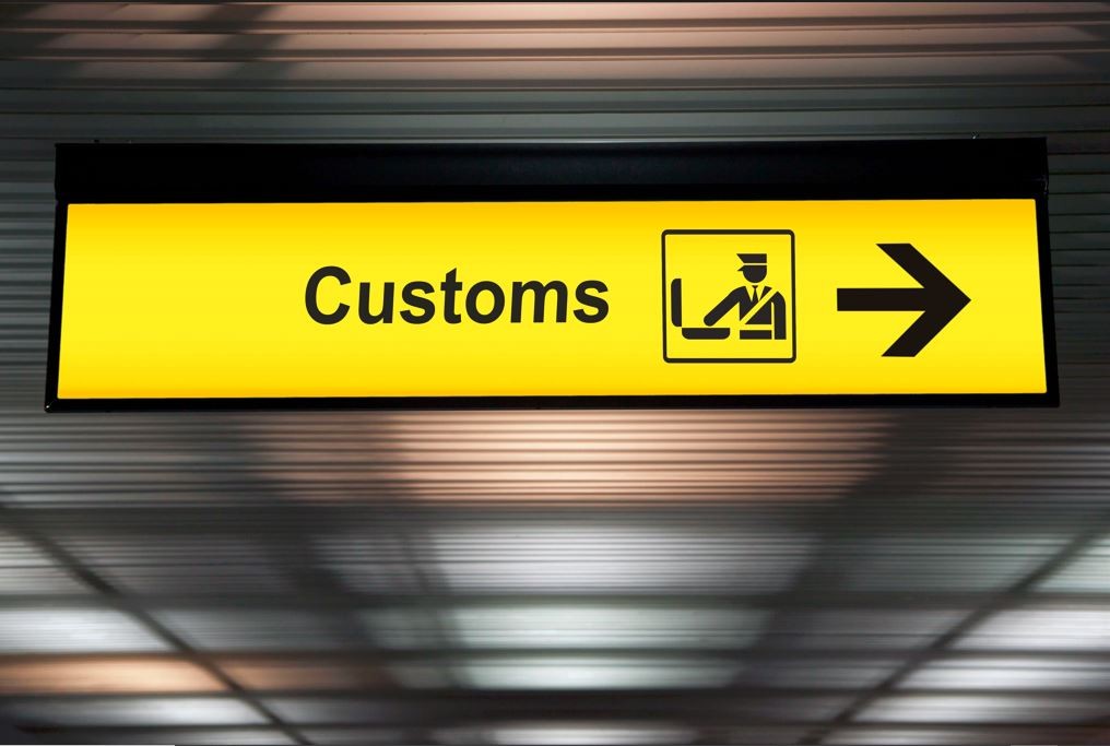 Cartel amarillo de un aeropuerto en el que se indica la palabra "Customs"