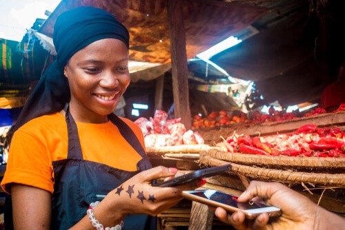 Una mujer africana paga un producto con el móvil en un mercado